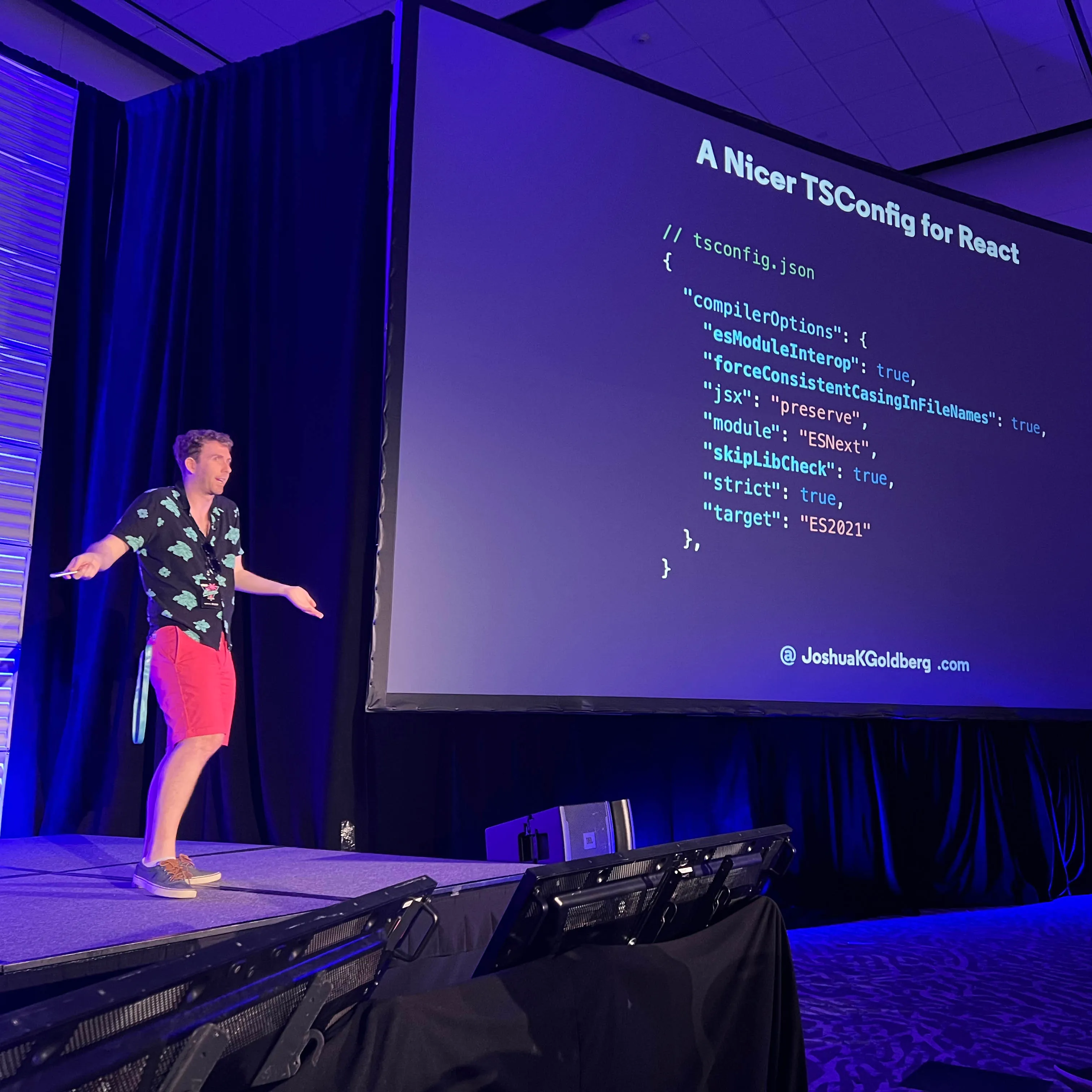 Josh smiling and gesturing on stage and giving a presentation showing the "Type Checking React (v2)" from the linked slides.